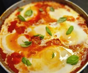 Israelsk shakshuka med æg i tomatsauce og friske basilikumblade
