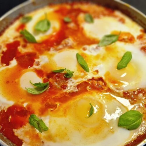Israelsk shakshuka med æg i tomatsauce og friske basilikumblade