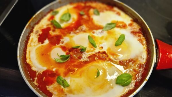 Israelsk shakshuka med æg i tomatsauce og friske basilikumblade