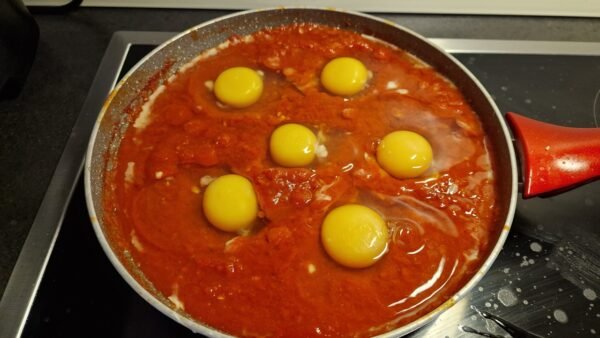 Seks rå æg slået ud i fordybninger i tomatsaucen