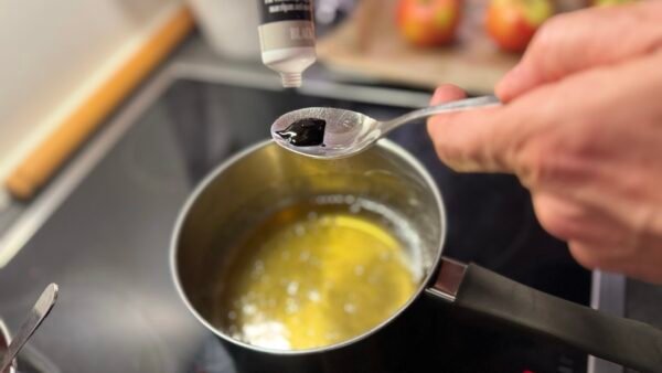 Sort frugtfarve måles op over en gryde med sukkerlage
