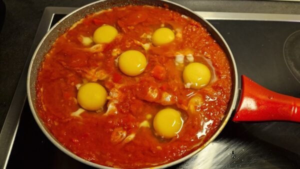 Seks æg slået ud i fordybninger i tomatsaucen